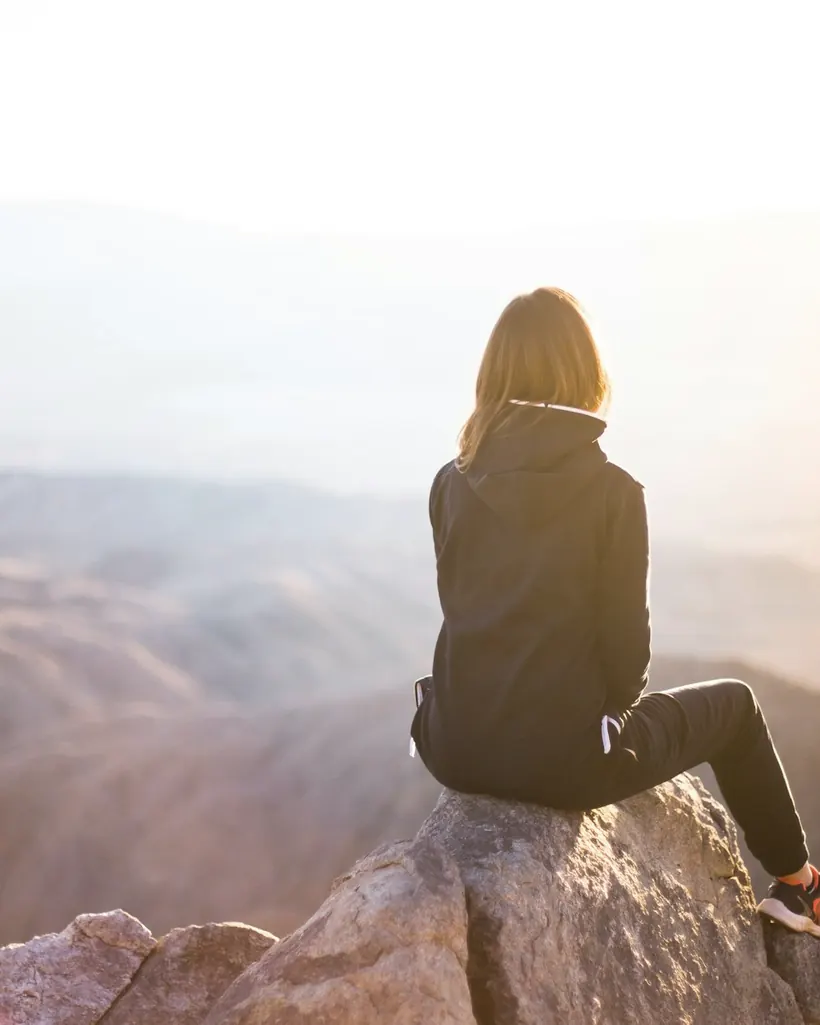 A person sitting quietly outdoors, looking out over a wide misty view